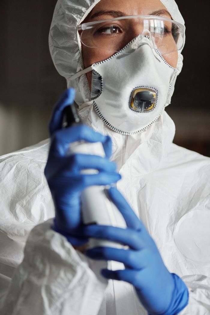about-04 Close-up of a woman in full protective gear holding a disinfectant spray.